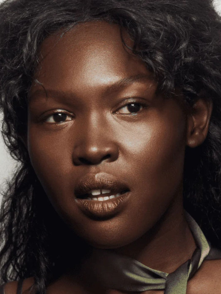 Close-up of a person with curly hair using 19/99 Beauty Cream Contour Stick in 'Kave' against a neutral background | Twentyseven Toronto