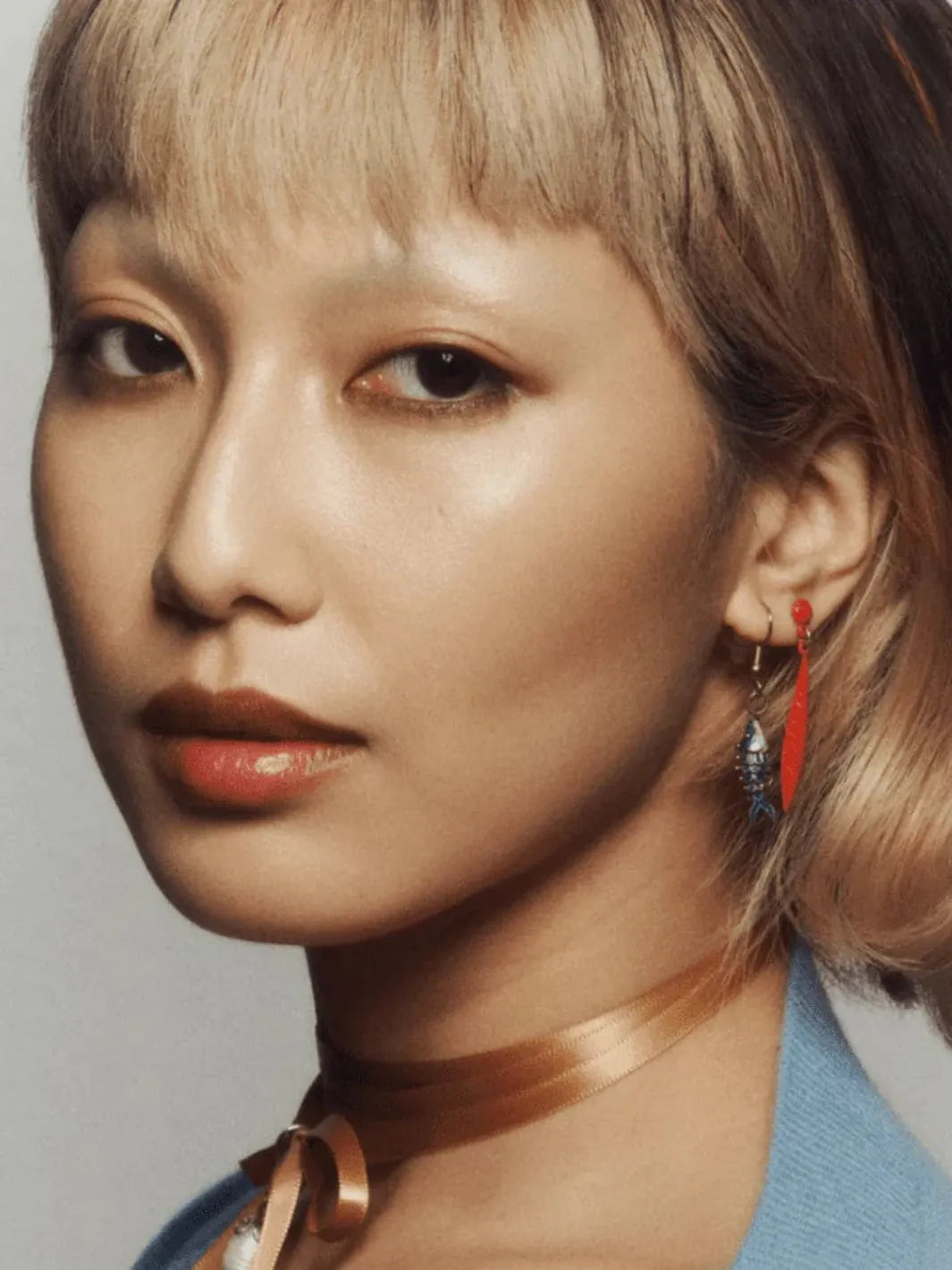 Close-up of a person with styled hair and earrings using 19/99 Beauty Cream Contour Stick in 'Tea' against a neutral background | Twentyseven Toronto