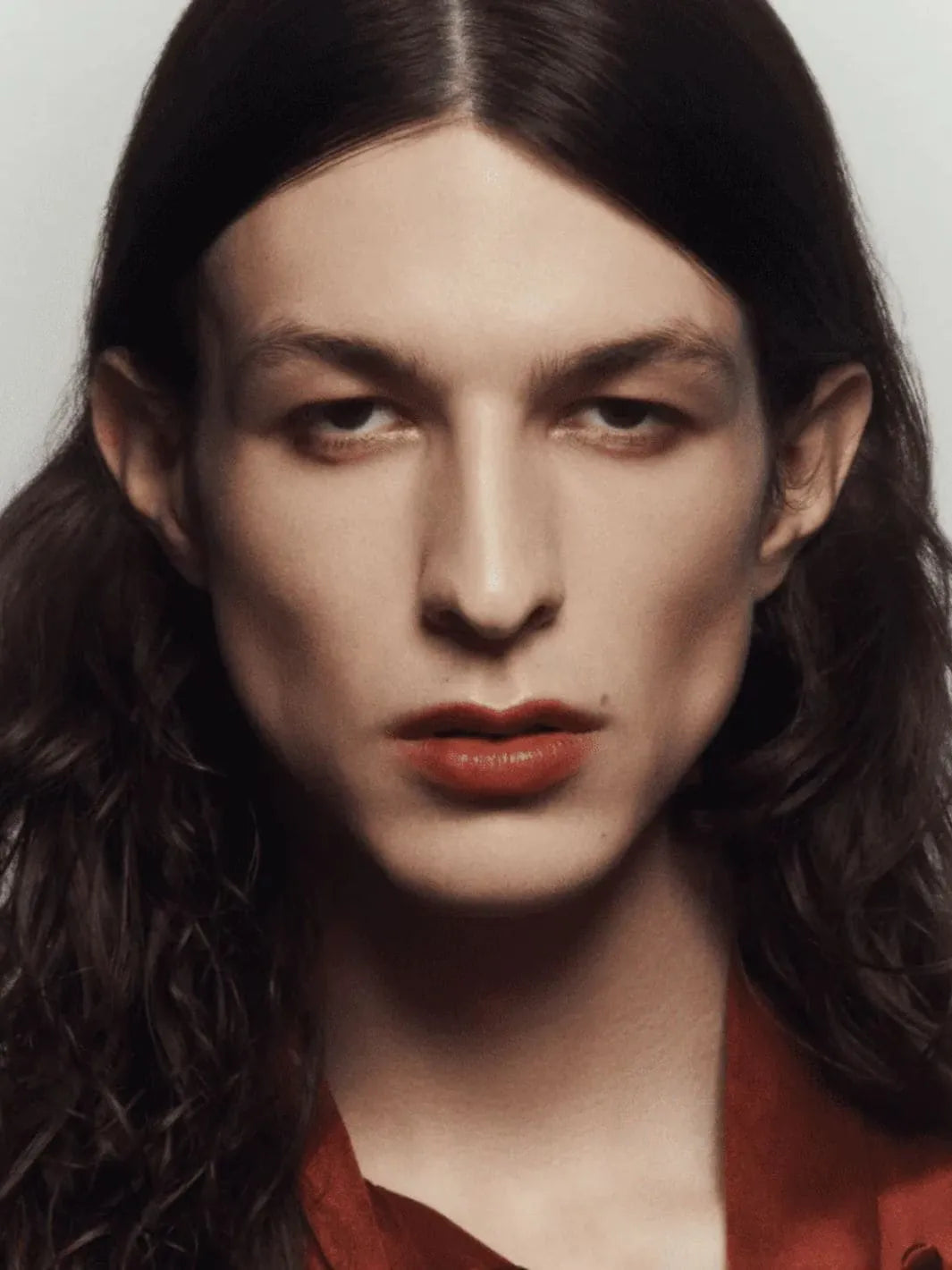 Person with long dark hair wearing a red garment using 19/99 Beauty Cream Contour Stick in 'Tea' against a neutral background | Twentyseven Toronto