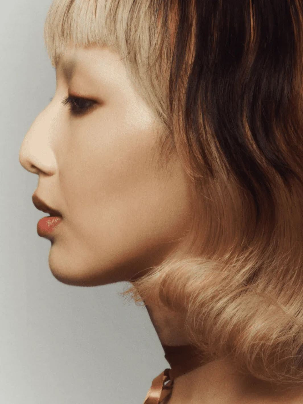 Side profile of a person with wavy hair using 19/99 Beauty Cream Highlight Stick in 'Perla' on a neutral background | Twentyseven Toronto