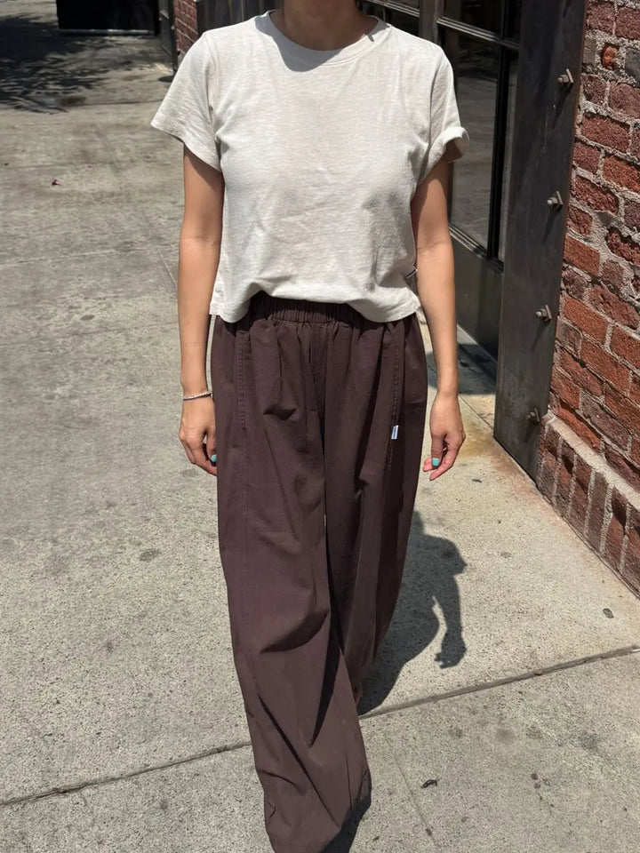 A full-length outdoor shot of a model walking down a sidewalk wearing the Le Bon Shoppe Airy Darling Tee in Rice with loose brown pants | Twentyseven