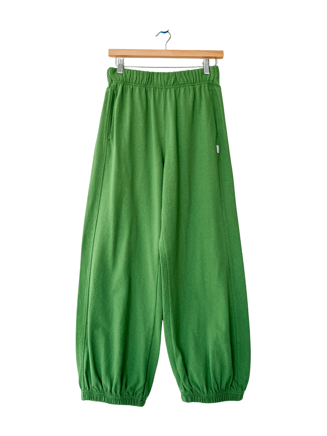 A studio product shot of the Le Bon Shoppe Balloon Pants in Asparagus hanging on a wooden clip hanger | Twentyseven