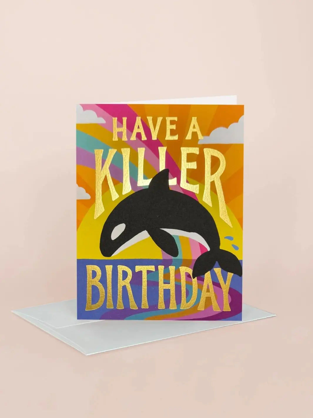 An angled lifestyle shot of the Idlewild Co. Birthday Greeting Card - Killer Birthday standing upright next to its white envelope against a soft beige background, highlighting the shiny gold foil text "Have a Killer Birthday" | Twentyseven
