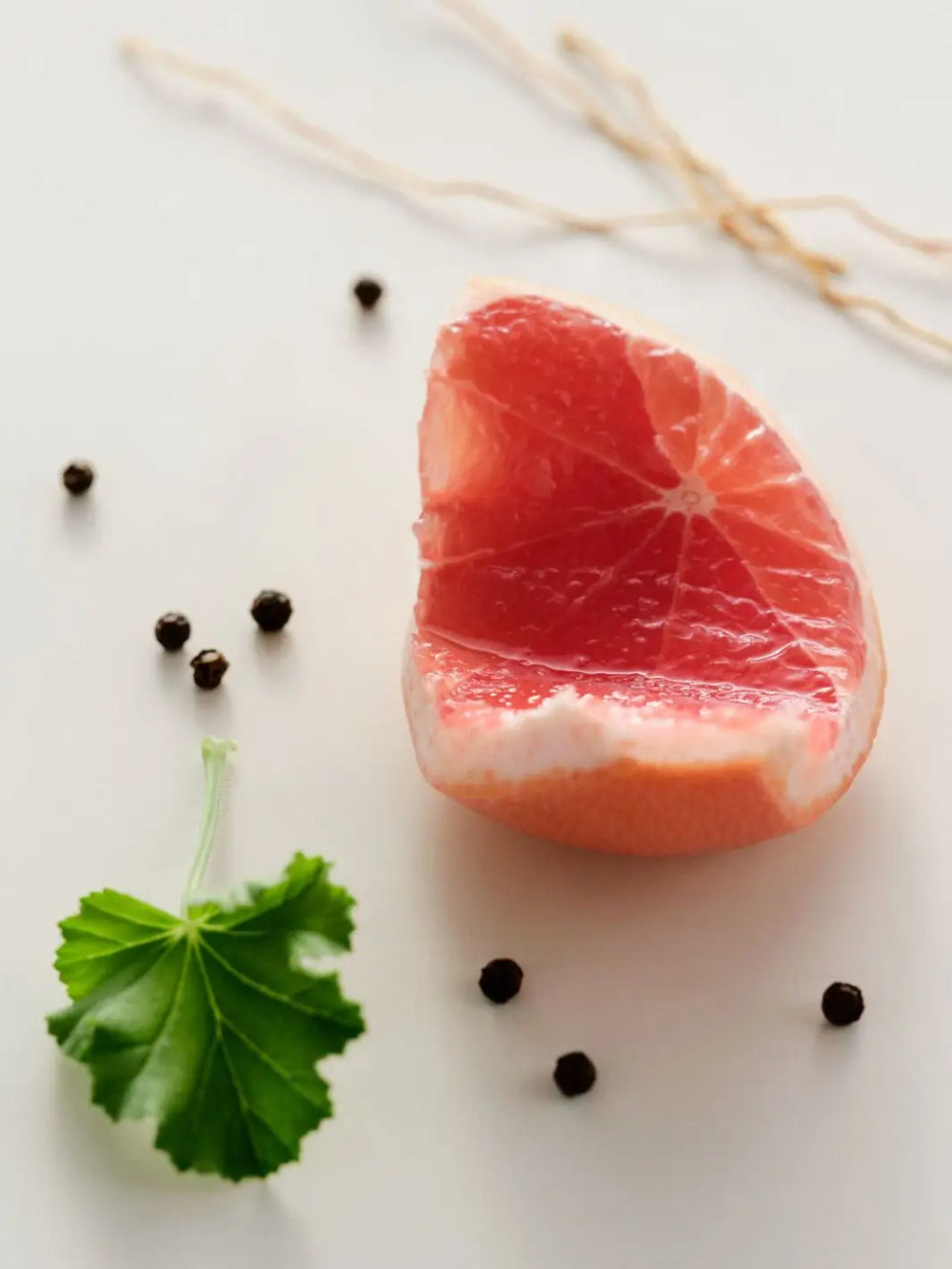 Sliced grapefruit with peppercorns and a leaf on a white surface to represent the ingredients for Maison Louis Marie No. 09 Vallée de Farney Body Lotion | Twentyseven