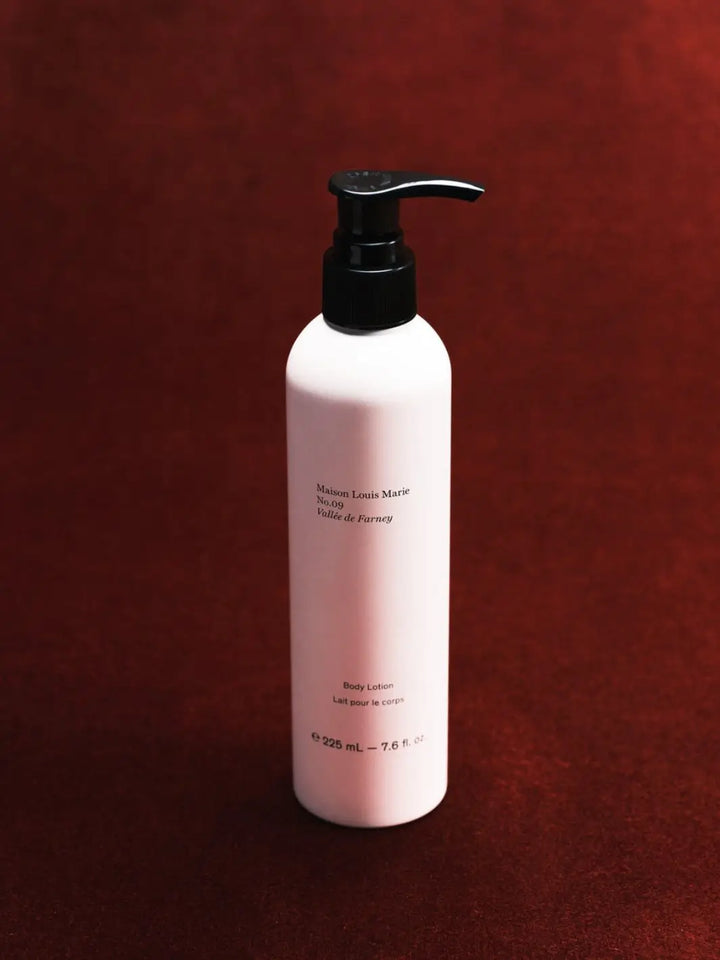 A 325 mL bottle of body lotion by Maison Louis Marie in Vallée de Farney, featuring a matte white bottle and a black pump dispenser, set against a dark textured red background | Twentyseven