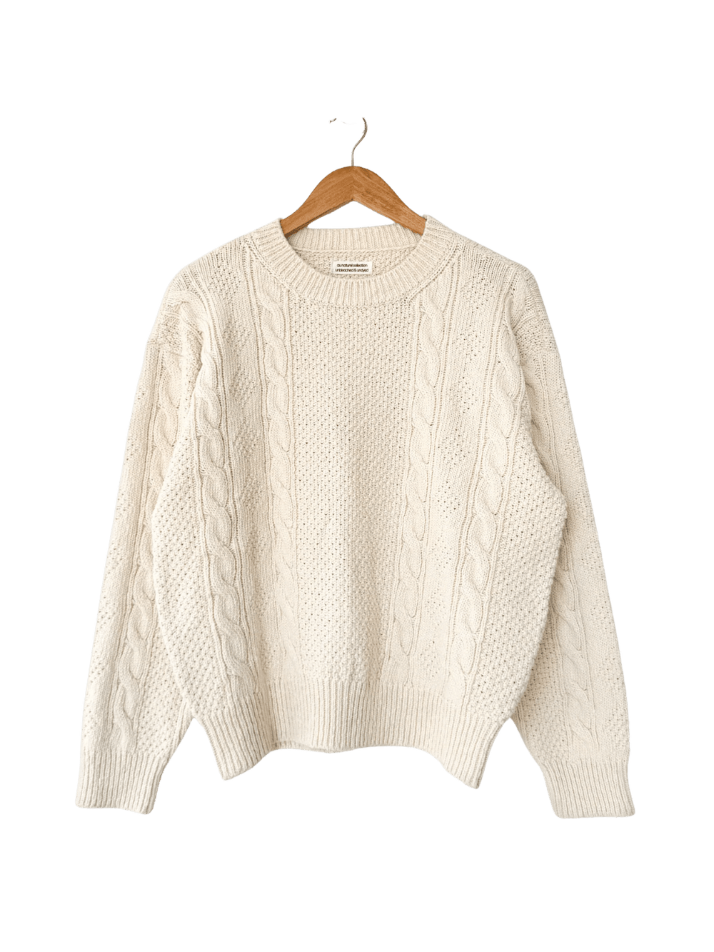 A flat lay product shot of the Le Bon Shoppe Cotton Fisherman Sweater in Naturel displayed on a wooden hanger | Twentyseven