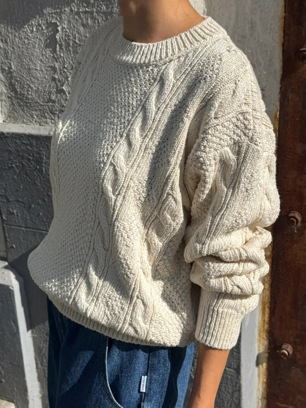 A side profile shot of a model wearing the Le Bon Shoppe Cotton Fisherman Sweater in Naturel highlighting the cable knit patterns on the sleeve | Twentyseven