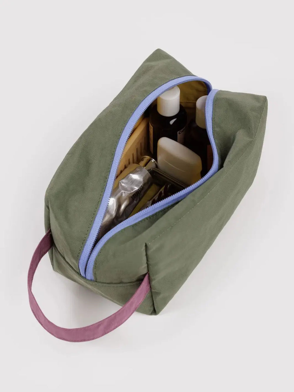 A top-down view of an open dark green BAGGU Dopp Kit in Caper Mix filled with assorted travel toiletries | Twentyseven