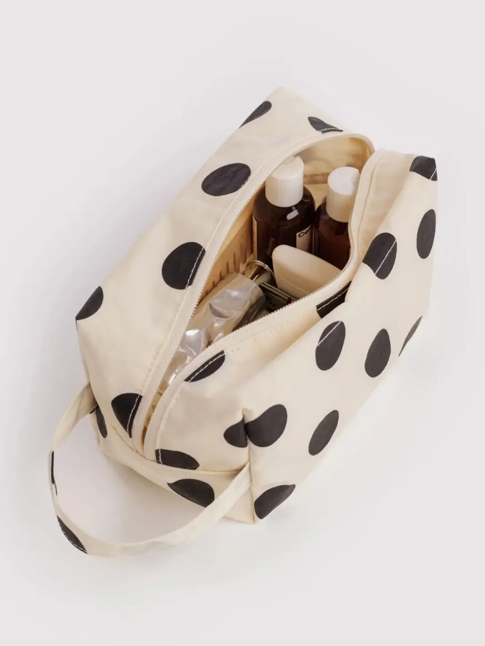 A top-down view of an open BAGGU Dopp Kit in Cream and Black Polka Dot filled with various travel toiletries | Twentyseven