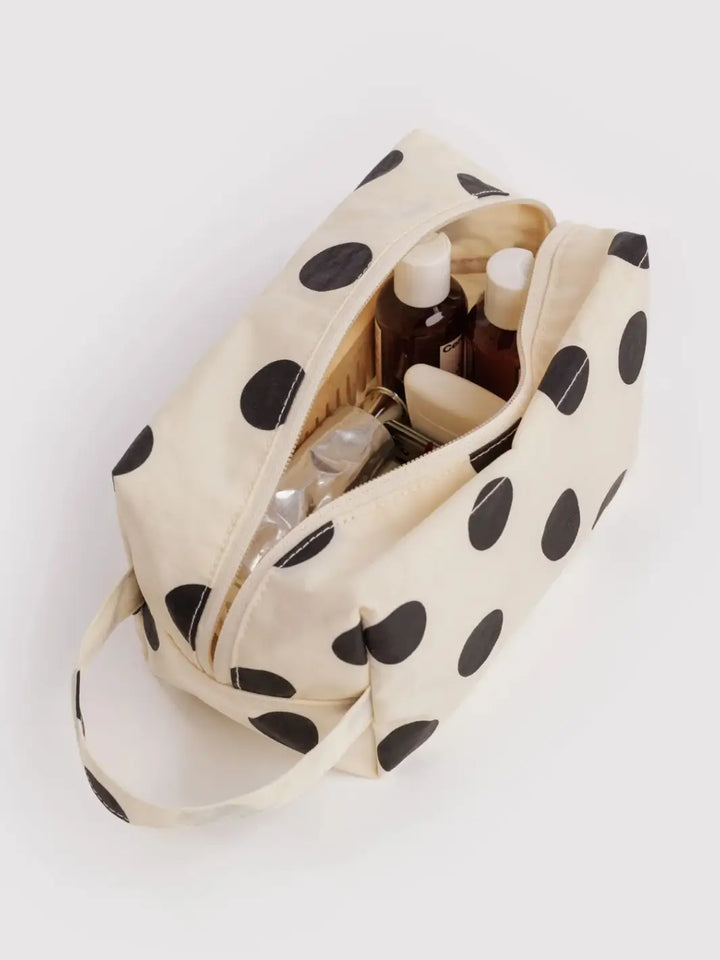 A top-down view of an open BAGGU Dopp Kit in Cream and Black Polka Dot filled with various travel toiletries | Twentyseven