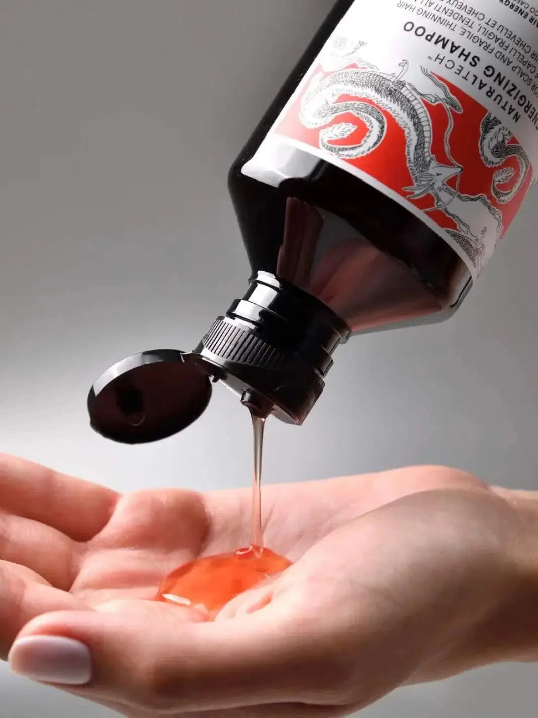 An amber bottle is tilted to pour a translucent, orange-tinted gel shampoo onto an open palm, showcasing a product from the Davines ENERGIZING Duo | Twentyseven Toronto