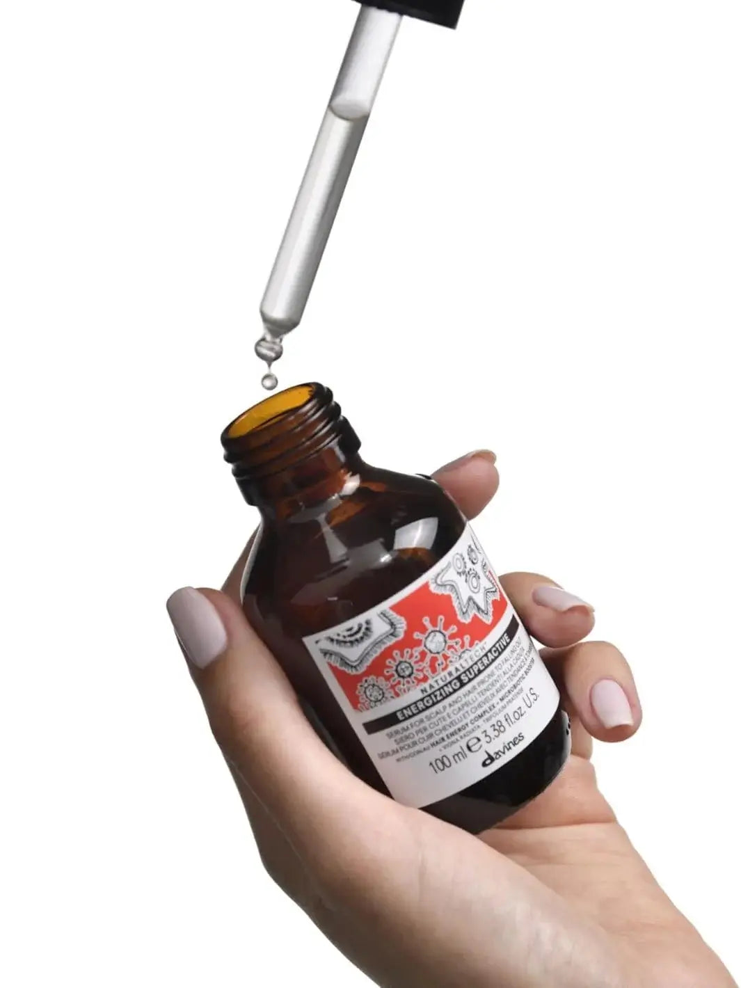 A hand holds an open amber bottle of Energizing Superactive serum while a glass dropper hovers above it, highlighting the targeted treatment from the Davines ENERGIZING Duo | Twentyseven Toronto