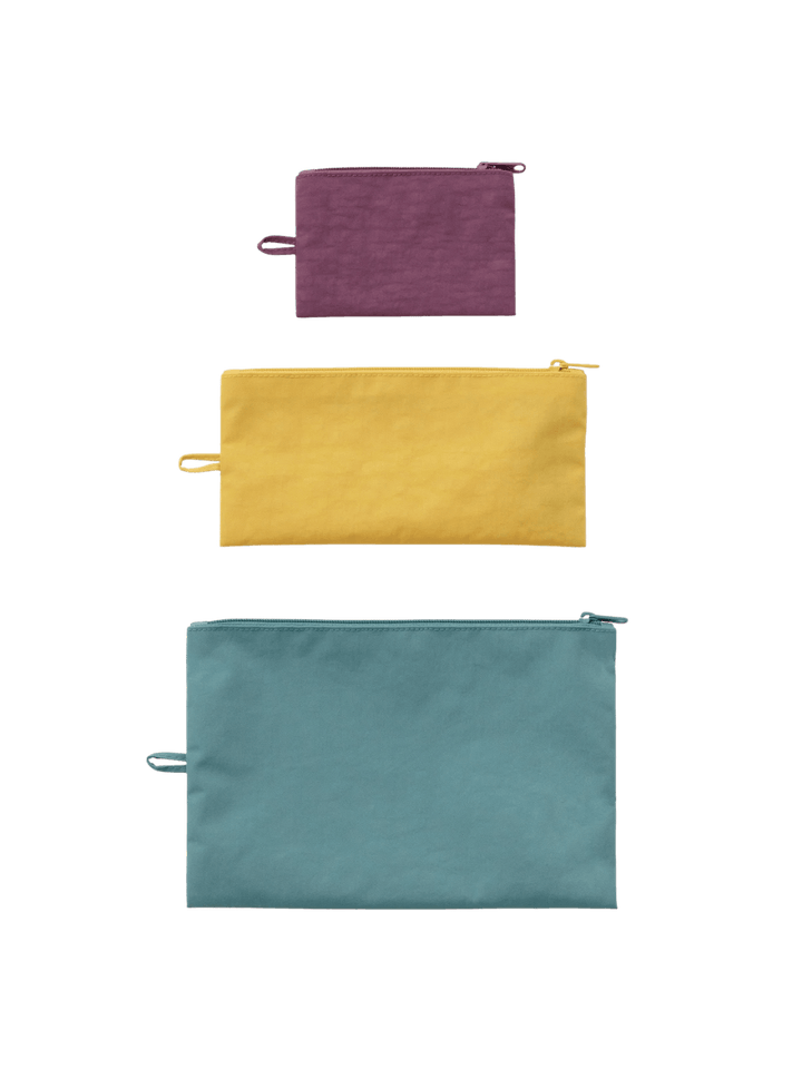 A top-down product shot of the BAGGU Flat Pouch Set in Jewel Mix featuring small purple, medium yellow, and large teal zippered pouches lined up vertically | Twentyseven