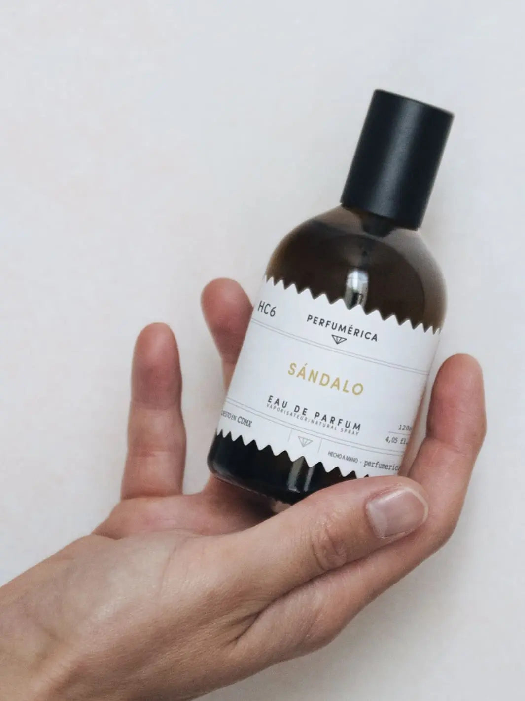 Hand holding perfume bottle with a black cap, the fragrance 'HC6 Sandalwood Eau de Parfum' from Perfumérica, 120ml, on a white background | Twentyseven Toronto