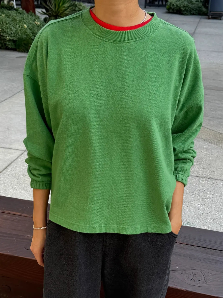 A front view of a model wearing the long-sleeve Le Bon Shoppe Naturelle Tee in Asparagus with a red collar layered underneath | Twentyseven