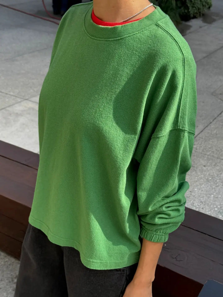 A side angle shot of a model wearing the green long-sleeve Le Bon Shoppe Naturelle Tee in Asparagus outdoors | Twentyseven