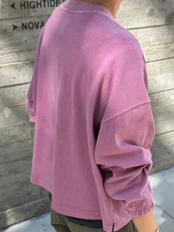 A back angle shot of a model wearing the Le Bon Shoppe Naturelle Tee in Dusty Lilac standing against a wooden wall background | Twentyseven