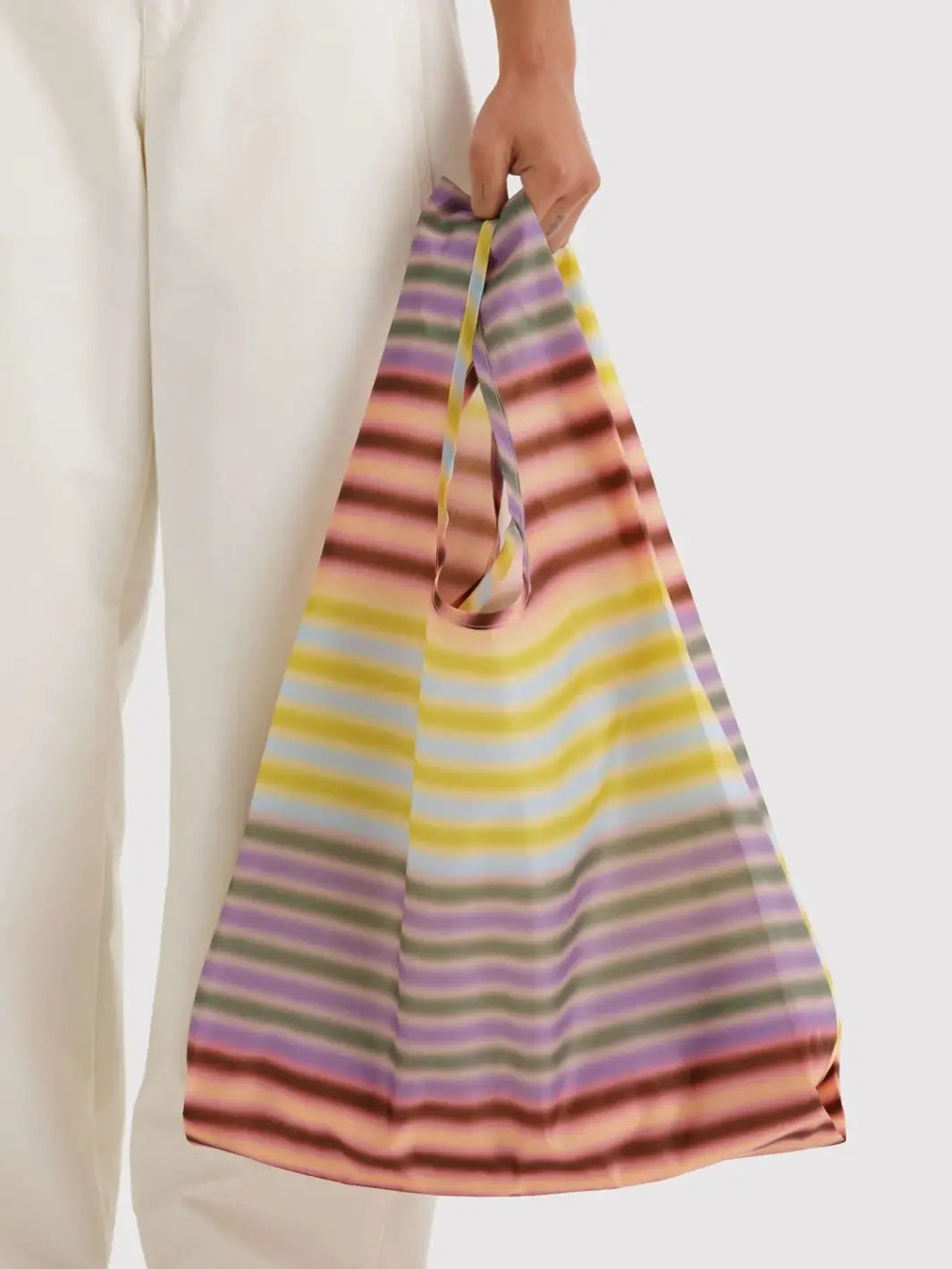 A model wearing white pants holding the BAGGU Standard Baggu in Gradient Stripe Multi by its handles | Twentyseven