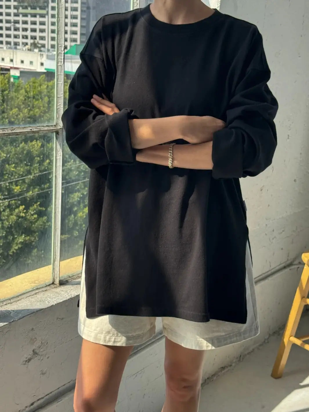 A model with arms crossed wearing the relaxed long-sleeve Le Bon Shoppe Sunday Tee in Black paired with light shorts near a window | Twentyseven