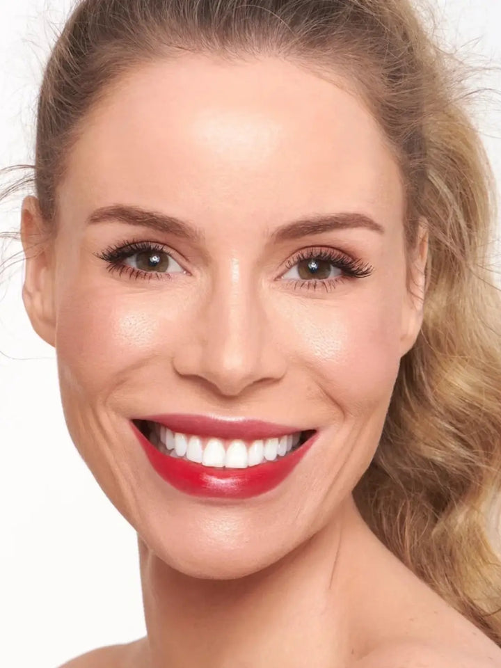A smiling blonde woman displaying a bold red finish from the Wonderskin WONDER BLADING Peel & Reveal Lip Color Kit - Romance | Twentyseven