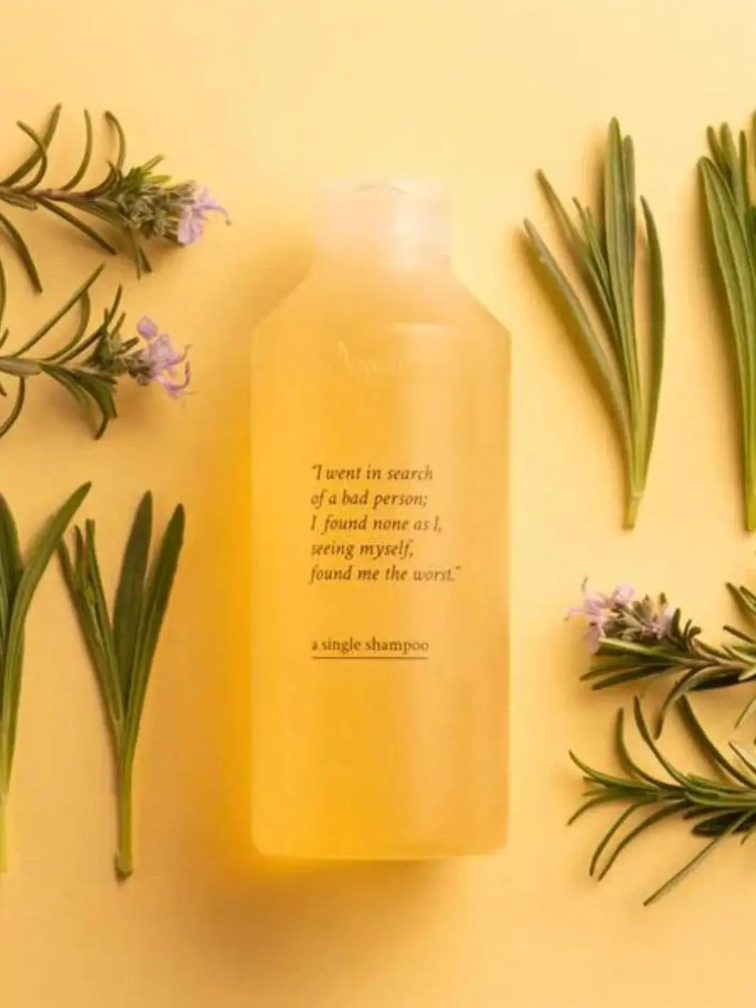 A bottle of Davines A Single Shampoo sits centered on a yellow surface surrounded by sprigs of rosemary and small purple flowers | Twentyseven Toronto