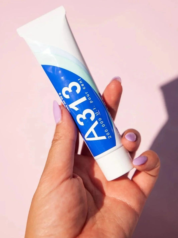 Hand holding a tube of A313 Vitamin A Retinol Cream against a pink background | Twentyseven Toronto