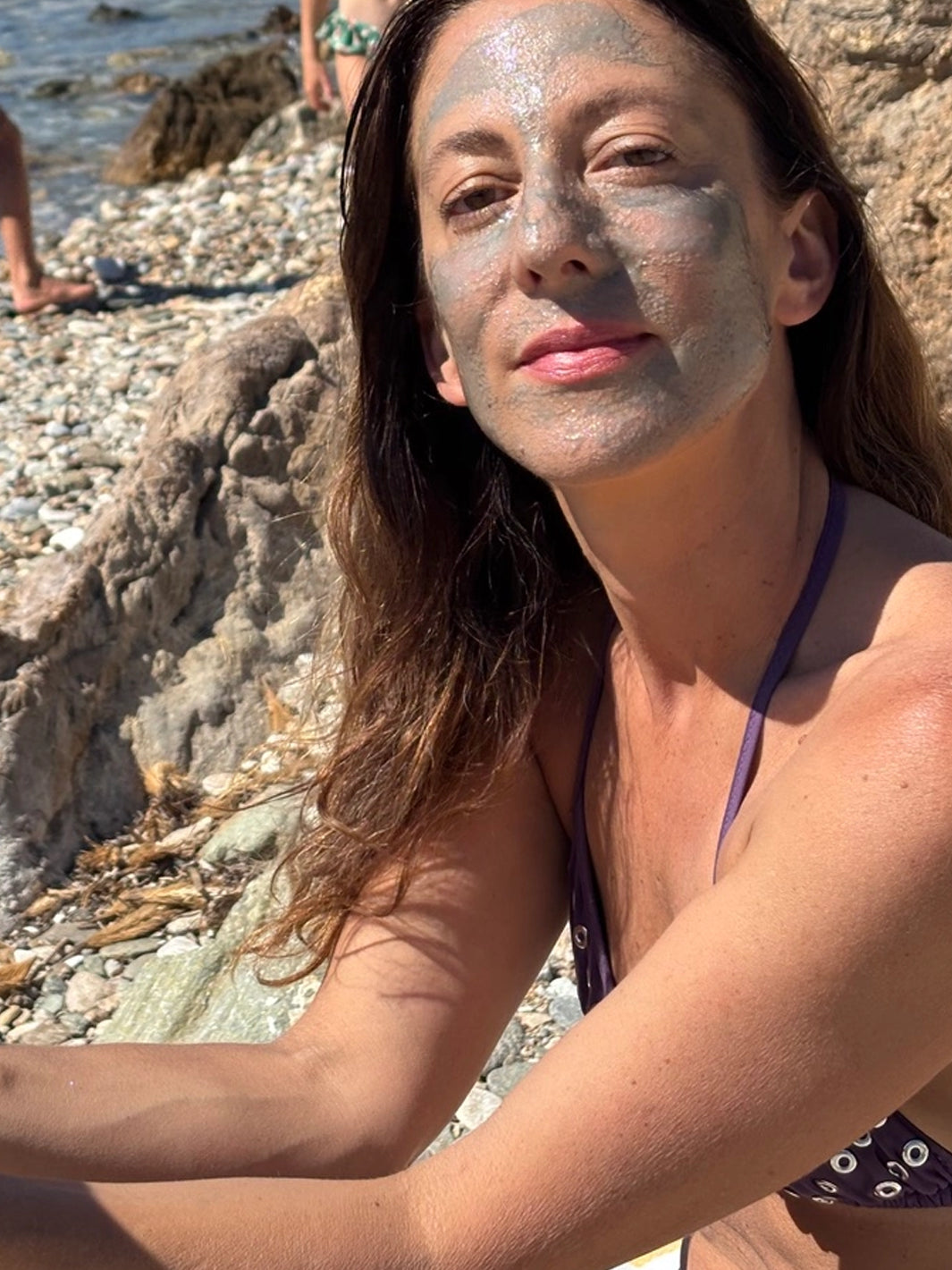 Woman wearing ACTIVIST Mānuka Honey Glacial Clay Mask while sitting on a rocky beach | Twentyseven Toronto