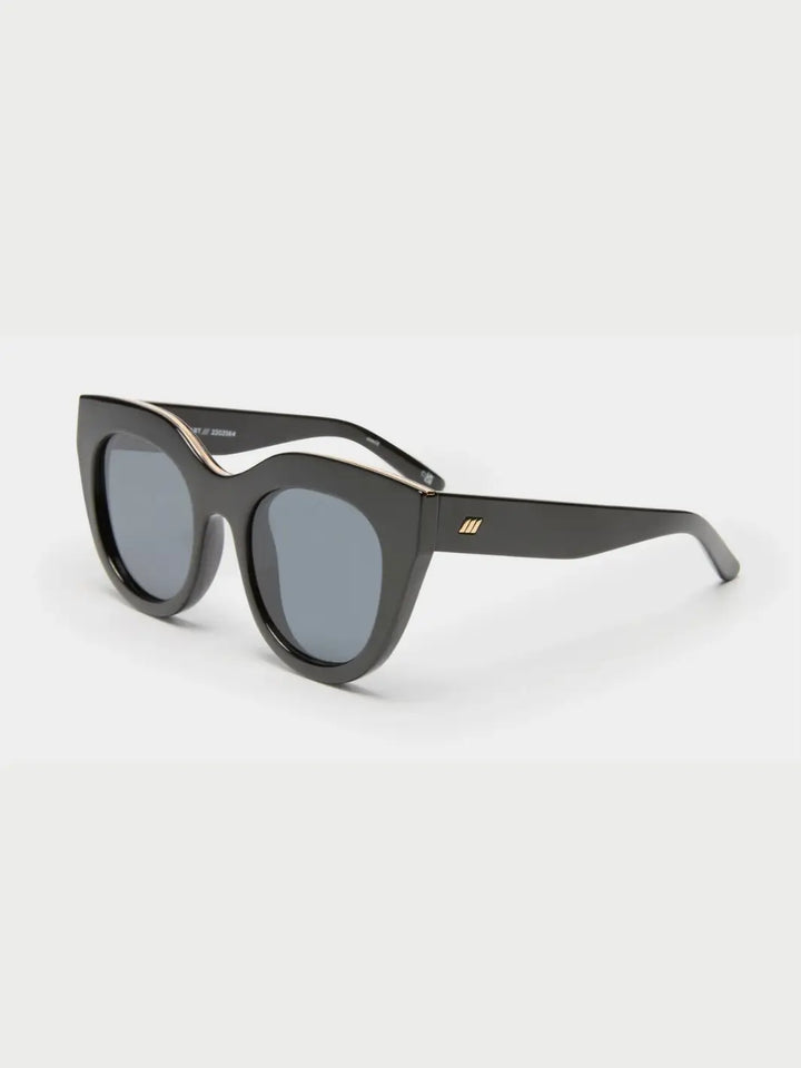 A three-quarter studio shot of the Le Specs Air Heart - Black sunglasses showcasing their glossy black cat-eye frame, grey lenses, and gold inlay detailing along the top rim | Twentyseven Toronto