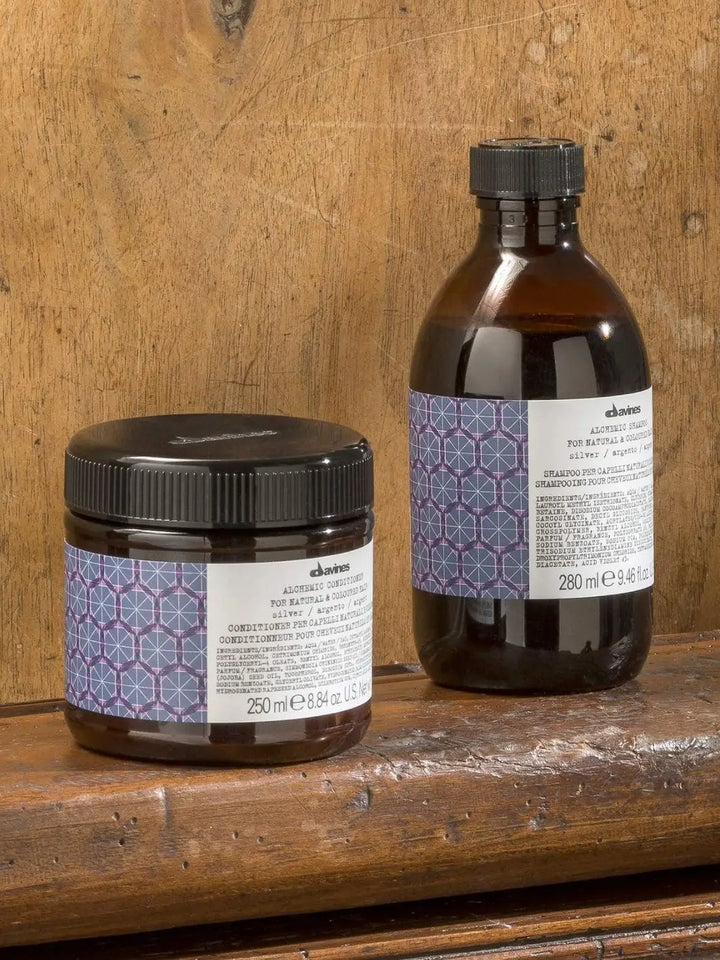 A round jar of conditioner and a bottle of Davines ALCHEMIC Silver Shampoo sit side-by-side on a rustic, weathered wood surface | Twentyseven Toronto