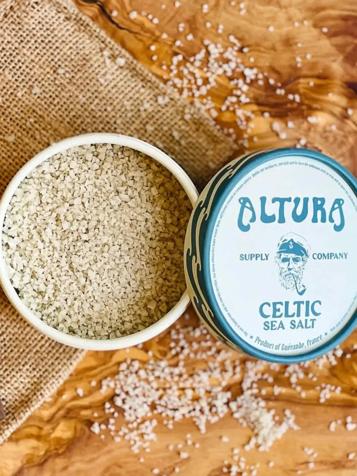 An overhead view displays an open tube of Altura Celtic Sea Salt on a wooden surface next to a burlap cloth, with scattered salt grains surrounding the packaging | Twentyseven Toronto