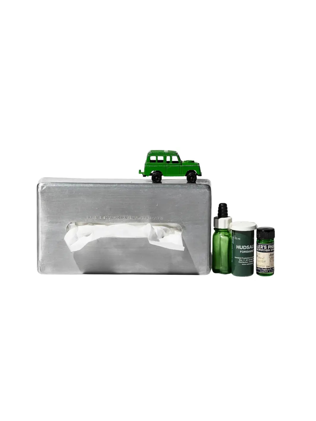 A small green toy truck sits on top of the Aluminum Tissue Case from Puebco, which is arranged next to a few small green apothecary bottles | Twentyseven Toronto