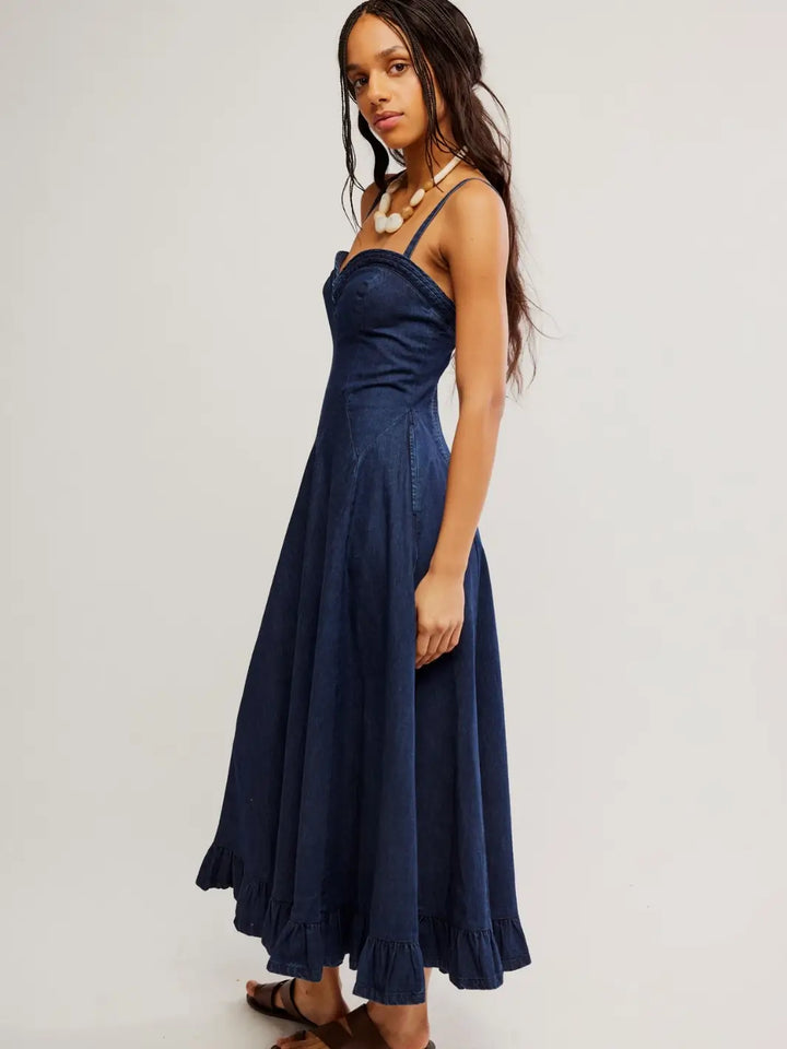 A side three-quarter view of a model wearing the Free People Another Season Denim Midi Dress in Rinse, showcasing its ruffled hemline and dark wash denim fabric | Twentyseven Toronto
