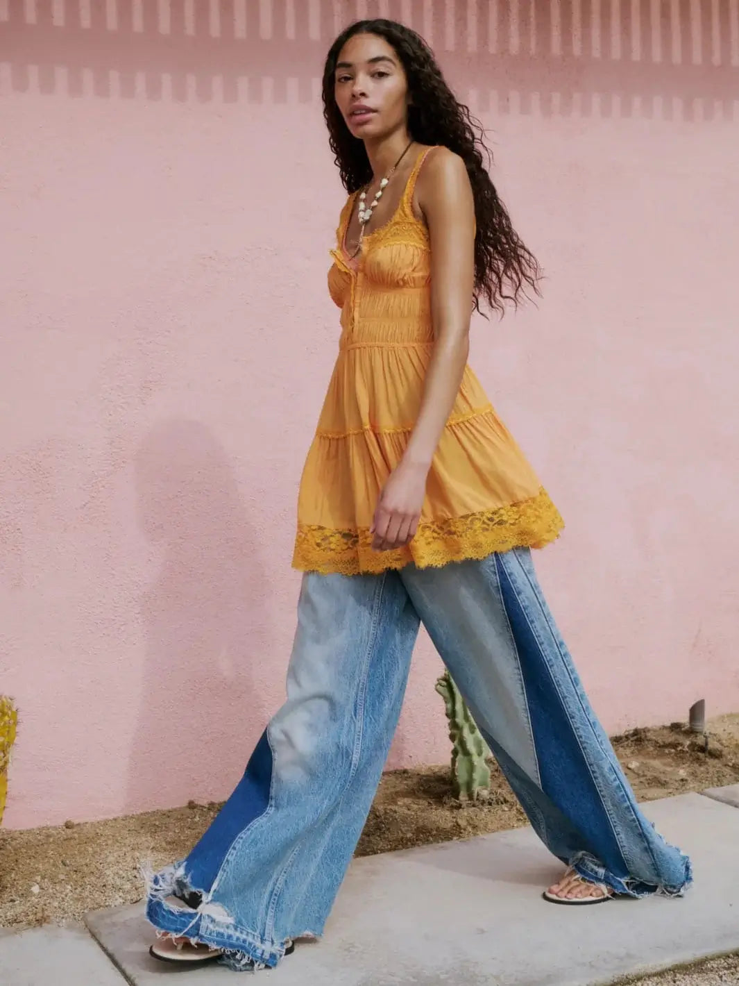 A model walks in front of a pink wall wearing the Free People Apollo Wide Leg in Streamline styled with a tiered yellow camisole top | Twentyseven Toronto