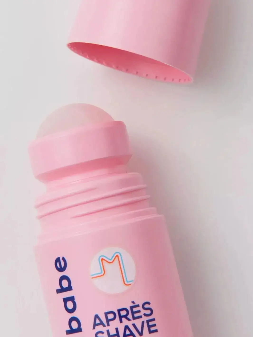 A close-up view displays an opened pink roll-on bottle against a white background, highlighting the convenient applicator design of Megababe Après Shave | Twentyseven Toronto