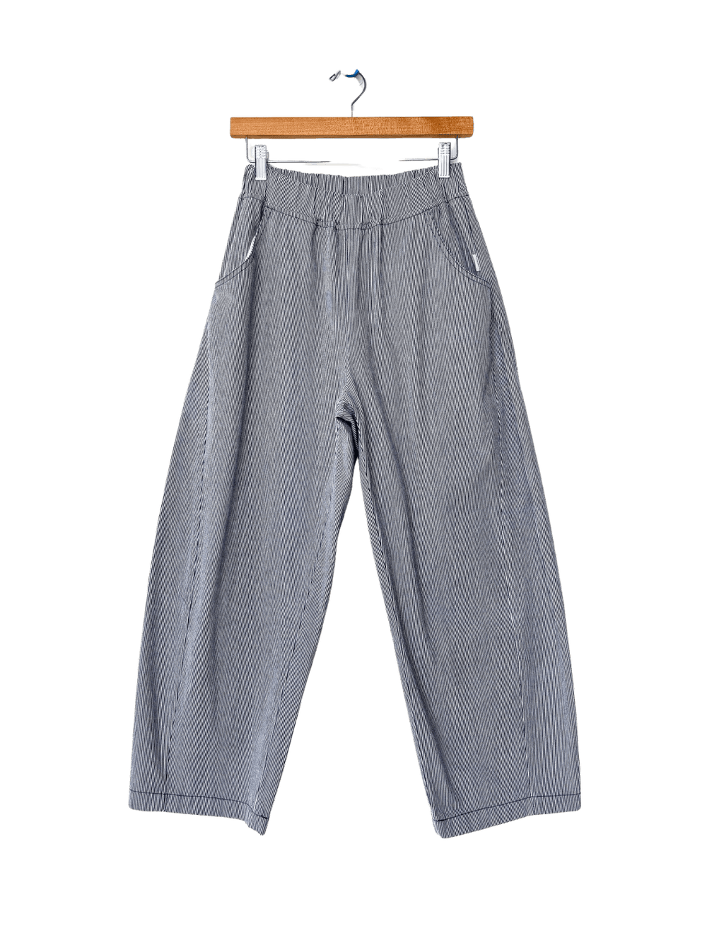 Grey and blue striped Le Bon Shoppe Arc Pants - Blue Stripe are shown straight-on, hanging from a wooden pants hanger with metal clips | Twentyseven Toronto