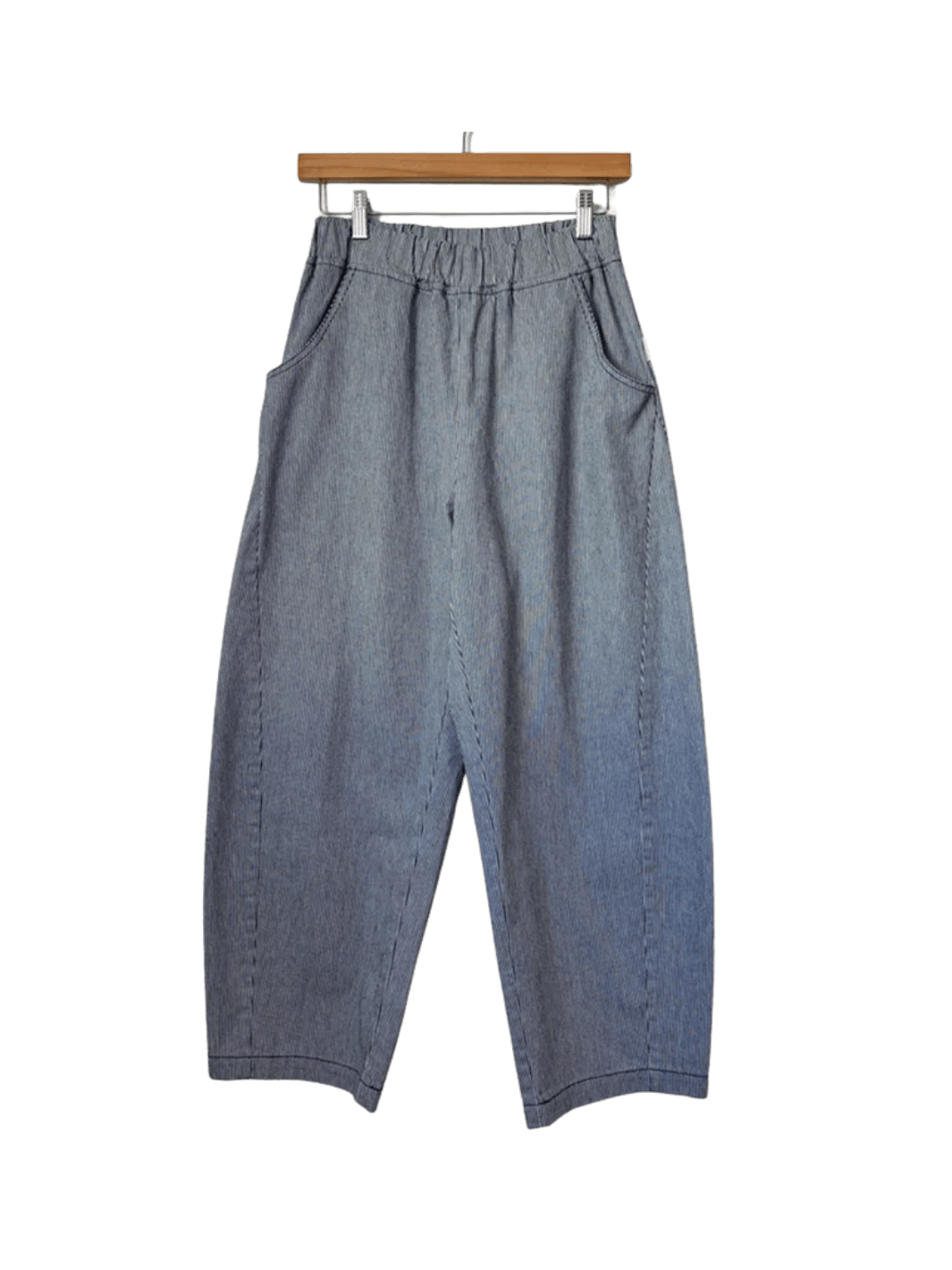 Grey and blue striped Le Bon Shoppe Arc Pants - Blue Stripe are shown straight-on, hanging from a wooden pants hanger with metal clips | Twentyseven Toronto