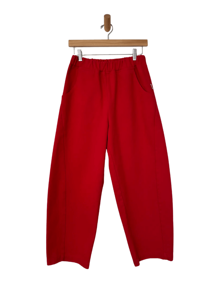 A flatlay product shot showcases the elastic waistband and structured, wide-leg design of the Le Bon Shoppe Arc Pants in Crayon Red hanging from a wooden hanger | Twentyseven Toronto