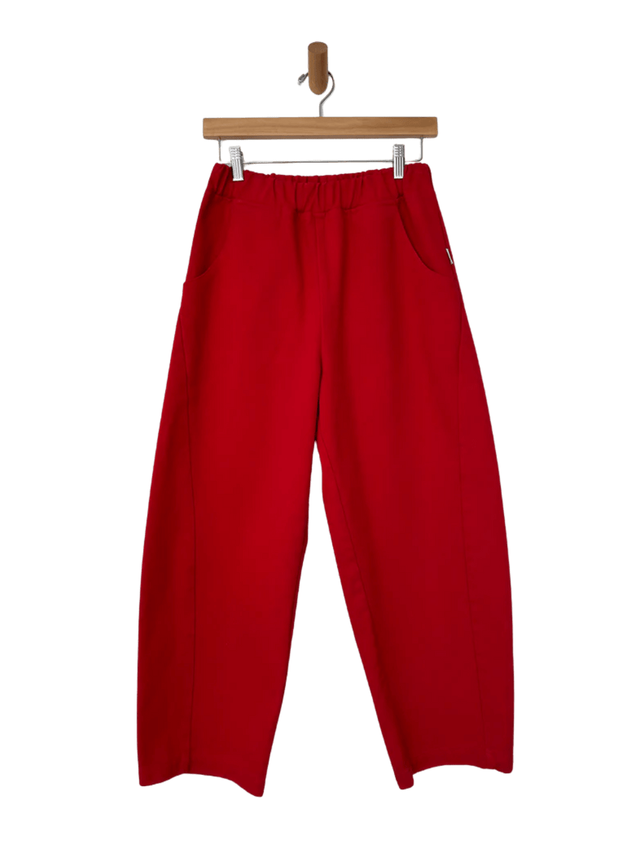 A flatlay product shot showcases the elastic waistband and structured, wide-leg design of the Le Bon Shoppe Arc Pants in Crayon Red hanging from a wooden hanger | Twentyseven Toronto