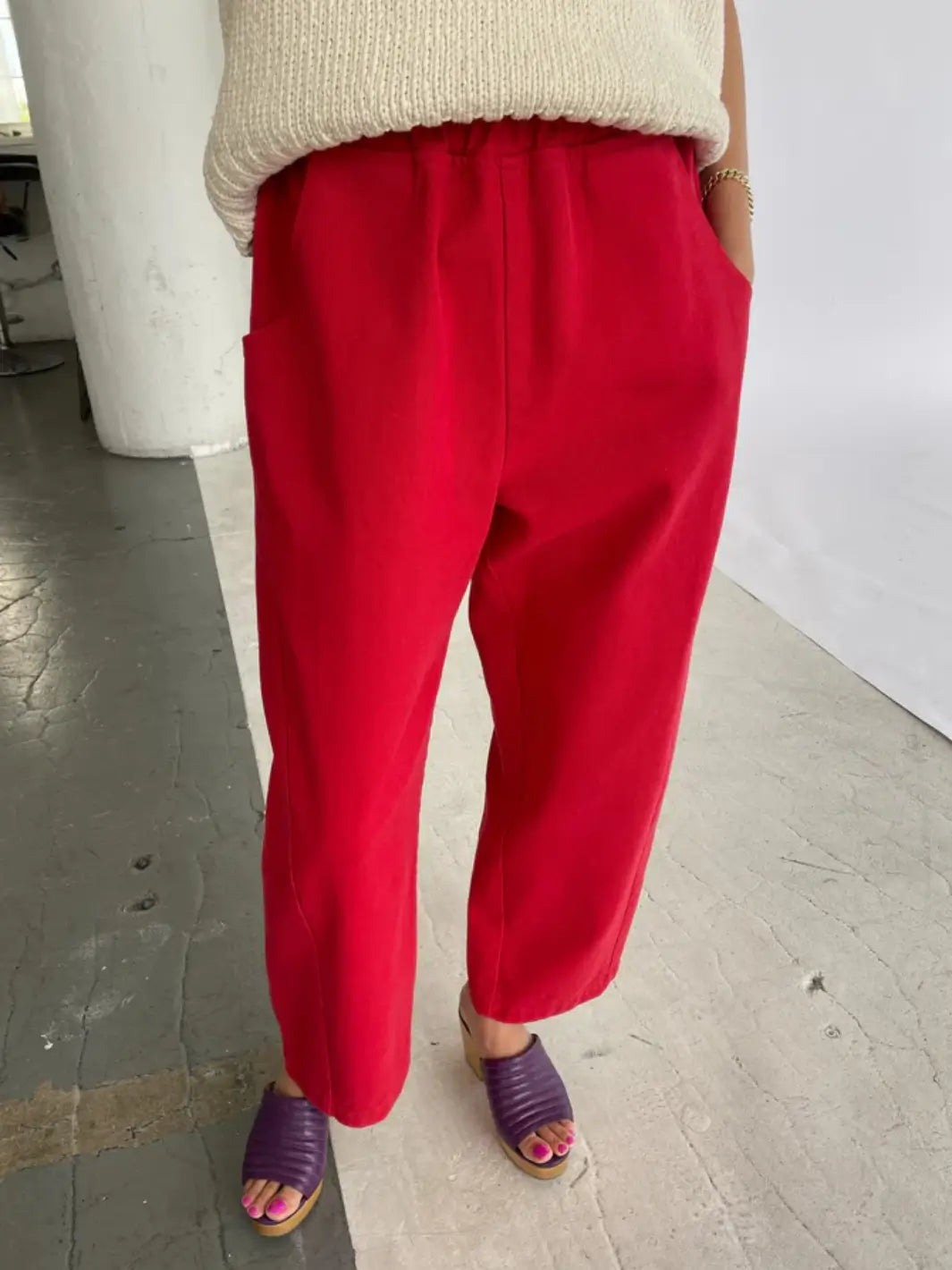 A front view shows a model wearing the vibrant Le Bon Shoppe Arc Pants in Crayon Red styled with a cream knit top and purple sandals | Twentyseven Toronto