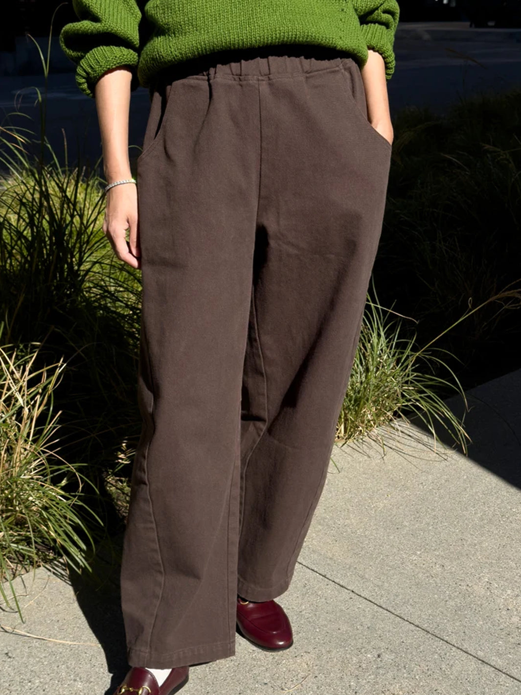 Model wearing umber brown wide-leg Arc Pants with an elastic waistband and side pockets, styled with a green knit sweater and burgundy loafers | Twentyseven Toronto
