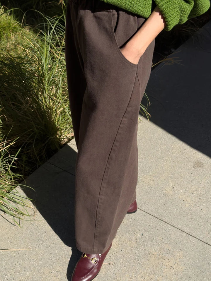 Side view of umber brown Arc Pants featuring a relaxed wide-leg silhouette and side pockets, styled with a green sweater and burgundy loafers | Twentyseven Toronto