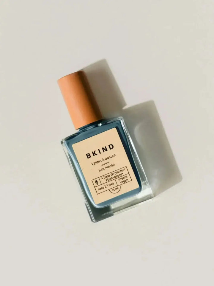 A square glass bottle of BKIND Nail Polish in Verdun Beach with a light beige cap rests diagonally against a clean, off-white background | Twentyseven Toronto