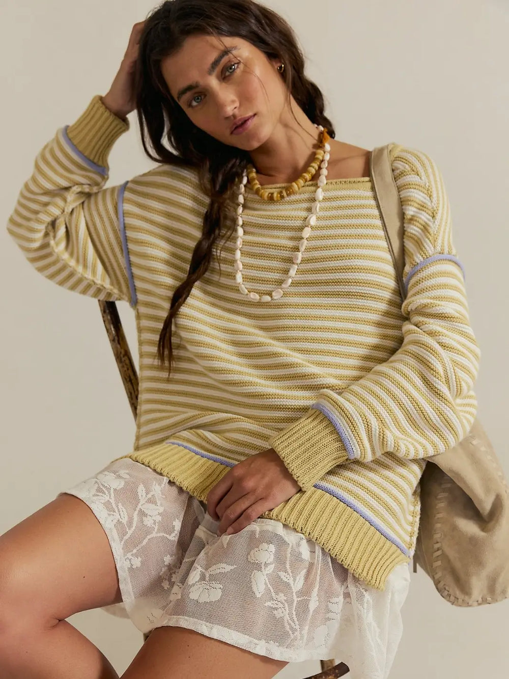 A model wearing the oversized, horizontally striped Free People We the Free Asher Pullover in Sand Combo styled with a white lace skirt and beaded necklaces | Twentyseven Toronto