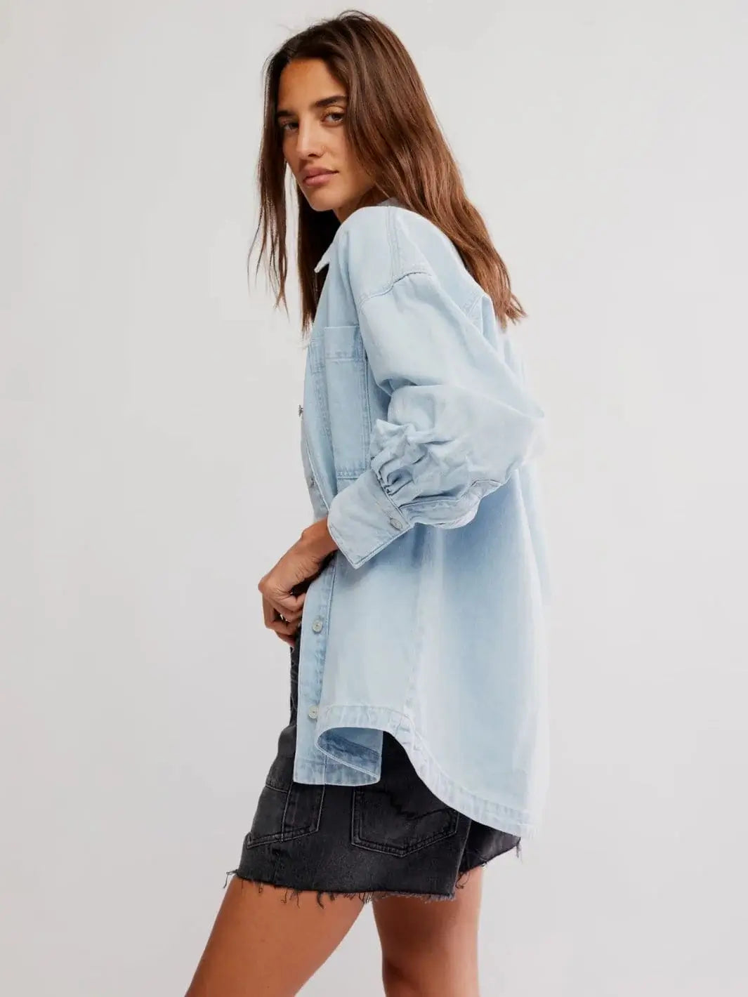 A side profile view highlights the dropped shoulders and curved high-low hemline of the Free People Ashley Denim Shirt - Classic Blue Wash | Twentyseven Toronto