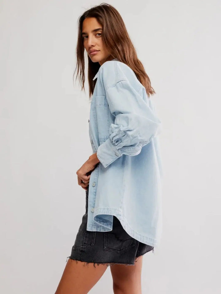 A side profile view highlights the dropped shoulders and curved high-low hemline of the Free People Ashley Denim Shirt - Classic Blue Wash | Twentyseven Toronto