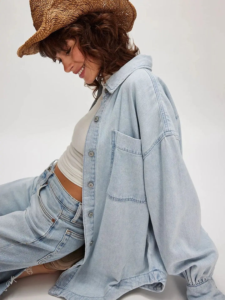 A model sits casually while wearing the Free People Ashley Denim Shirt - Classic Blue Wash paired with a straw cowboy hat and matching light-wash jeans | Twentyseven Toronto