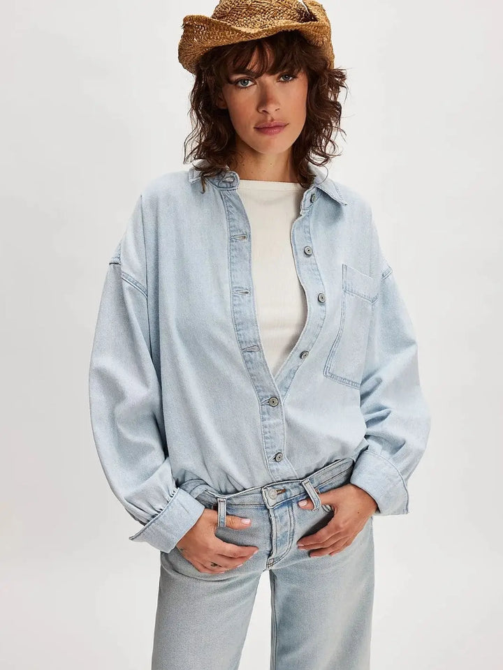 A model poses from the front with hands in her pockets, highlighting the classic collar and effortless drape of the Free People Ashley Denim Shirt - Classic Blue Wash | Twentyseven Toronto