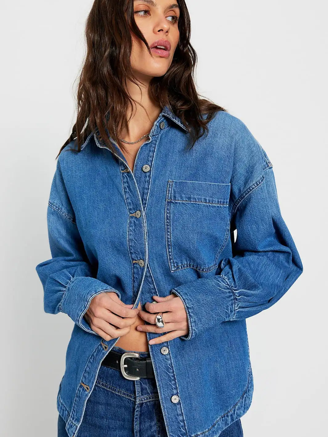 Woman wearing a blue denim shirt from Free People We the Free 'Ashley Denim Shirt' in 'Medium Wash' on a white background  | Twentyseven Toronto