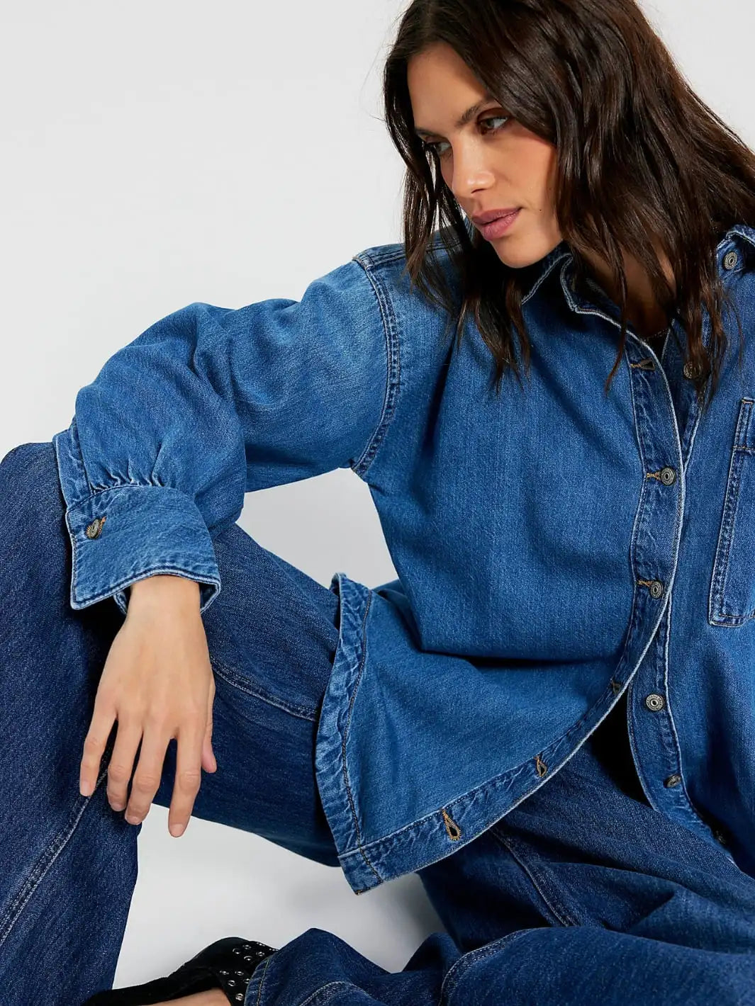 Woman sitting down wearing a blue denim shirt from Free People We the Free 'Ashley Denim Shirt' in 'Medium Wash' on a white background  | Twentyseven Toronto