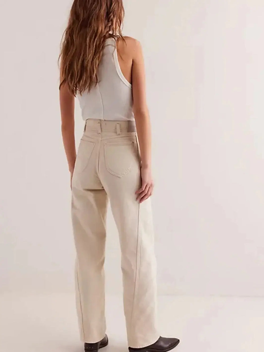 A view from behind shows a model wearing the high-waisted Free People Aster Straight-Leg Jeans - Cream featuring a relaxed straight-leg fit and pointed back pockets styled with dark boots | Twentyseven Toronto